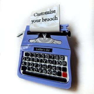 Spilla macchina da scrivere in plexiglass colorato, con tasti neri incisi e lettere dipinte a mano in bianco foglio piegato a mano, sul quale si può incidere una parola o frase